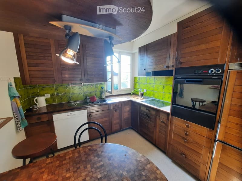 A cozy kitchen with wooden cabinets, a central island, and a dining area. Features include a sink, dishwasher, oven, and a small table with chairs.