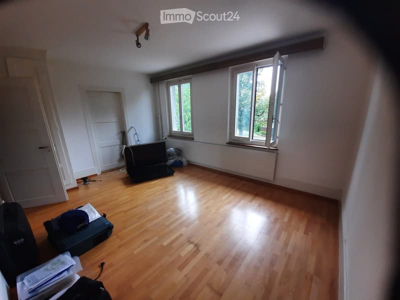 Empty room with wooden flooring, white walls, and large windows letting in natural light. No furniture or furnishings are present.