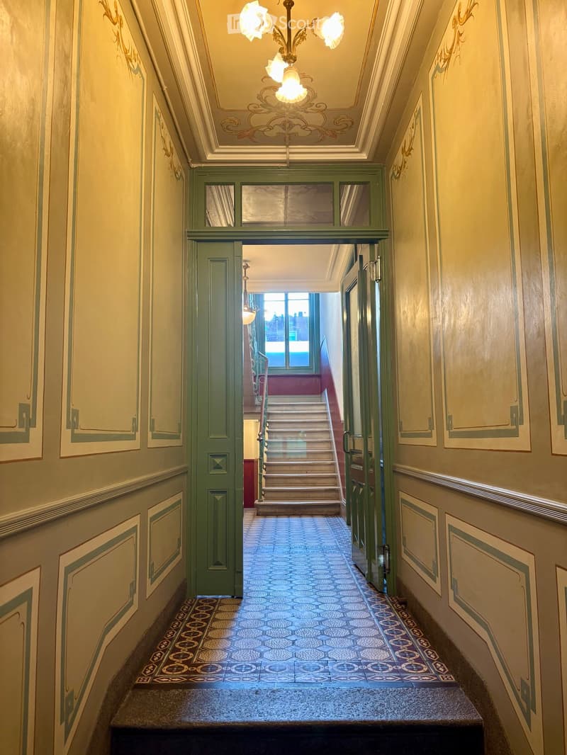 Elegant hallway with ornate wall decorations, a chandelier, and a patterned tile floor leading to a staircase.