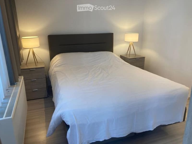 Modern bedroom with a large bed, two nightstands, lamps, and a radiator near the window.