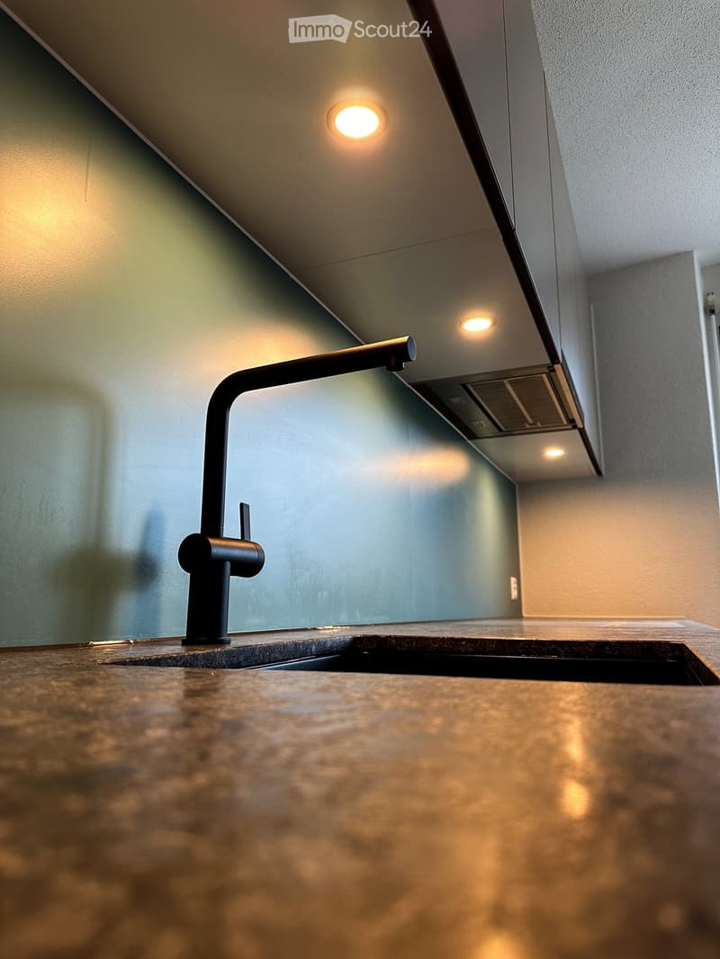 Modern kitchen sink with a sleek black faucet and a granite countertop, illuminated by recessed ceiling lights.