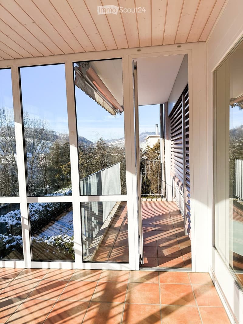 Bright, spacious balcony with large glass windows and doors, tiled floor, and scenic mountain view.