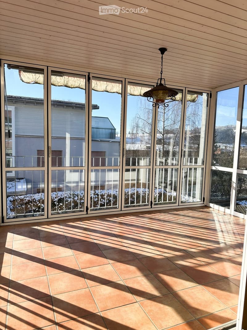 Spacious balcony with large glass sliding doors, tiled floor, and a hanging light fixture.