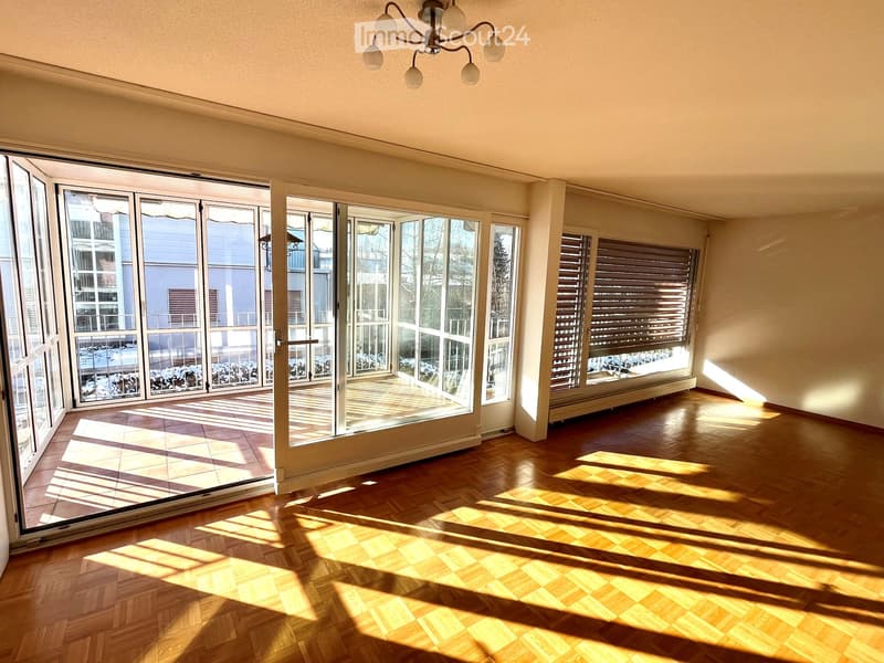 Empty room with wooden flooring, large windows, and sliding glass doors leading to a balcony. Natural light fills the space.