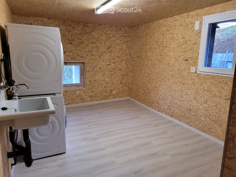Bathroom with wooden walls and floor, featuring a sink, faucet, and washing machine.