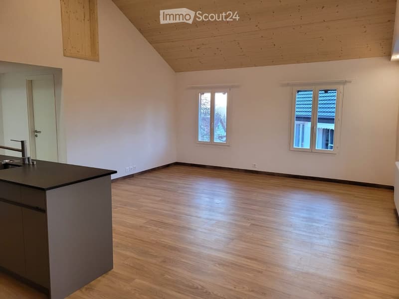 Empty room with wooden flooring, white walls, and a modern kitchen island with a sink and faucet. Two windows and a door are visible.