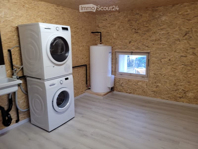 A small utility room with a stacked washer and dryer, a water heater, and a sink, all set against wooden panel walls.