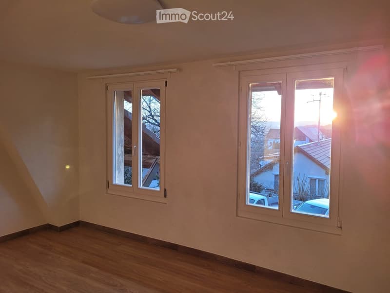 Empty room with wooden flooring, large windows, and natural light. No furniture or furnishings present.