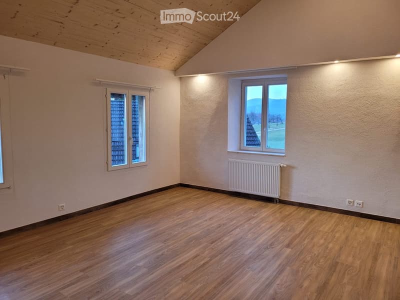 Empty room with wooden flooring, white walls, and two windows offering a view of the outside. A radiator is mounted on one wall.