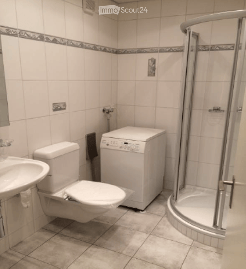 Modern bathroom with white tiles, a toilet, sink, shower, and a washing machine.