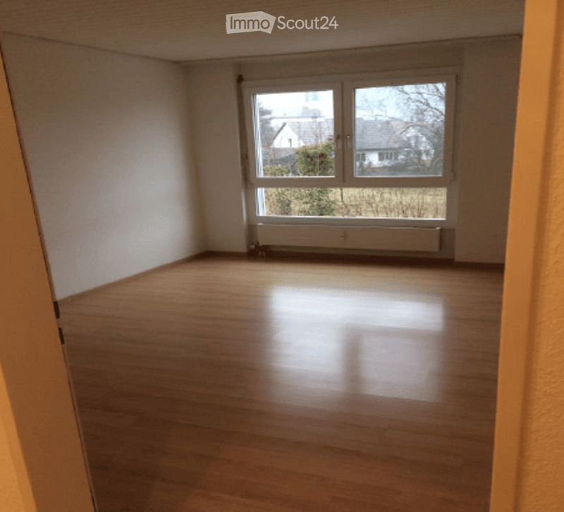 Empty room with wooden flooring, large window, radiator, and white walls.