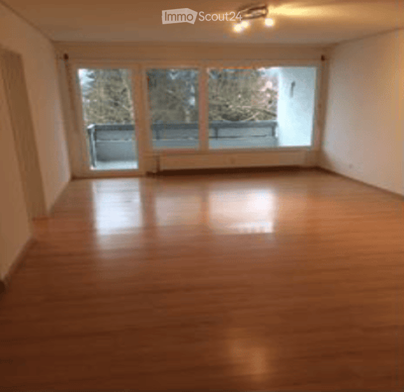Empty room with wooden flooring, large windows, and a sliding glass door leading to a balcony.