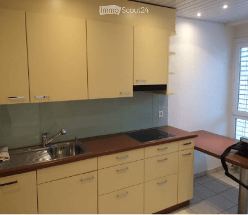 Bright kitchen with light yellow cabinets, stainless steel sink and faucet, dark countertop, and built-in stove. The space is clean and organized with a window providing natural light.