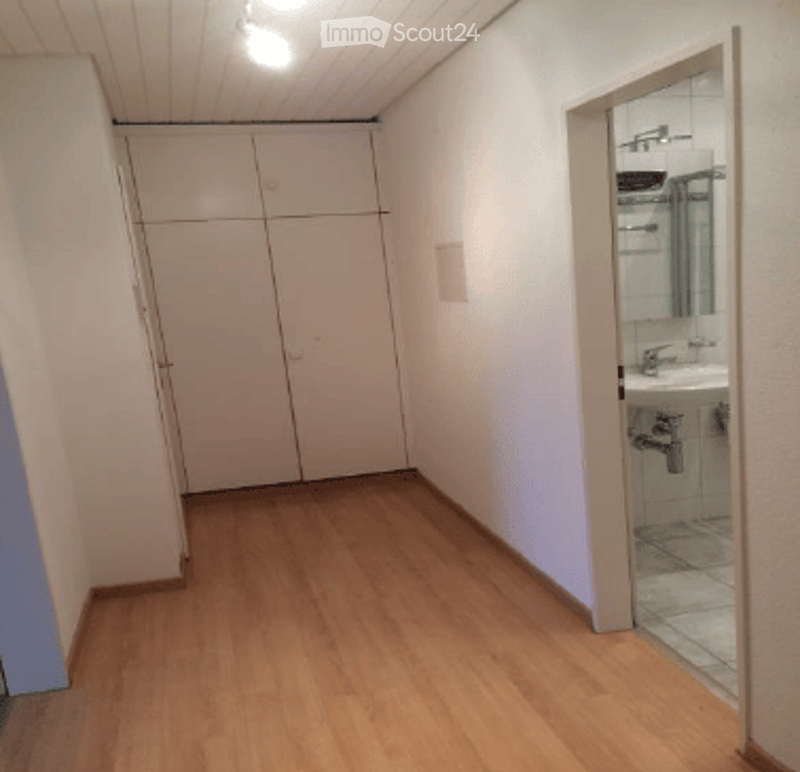 Empty room with wooden flooring, white walls, and a built-in closet. A small bathroom is visible through an open doorway.
