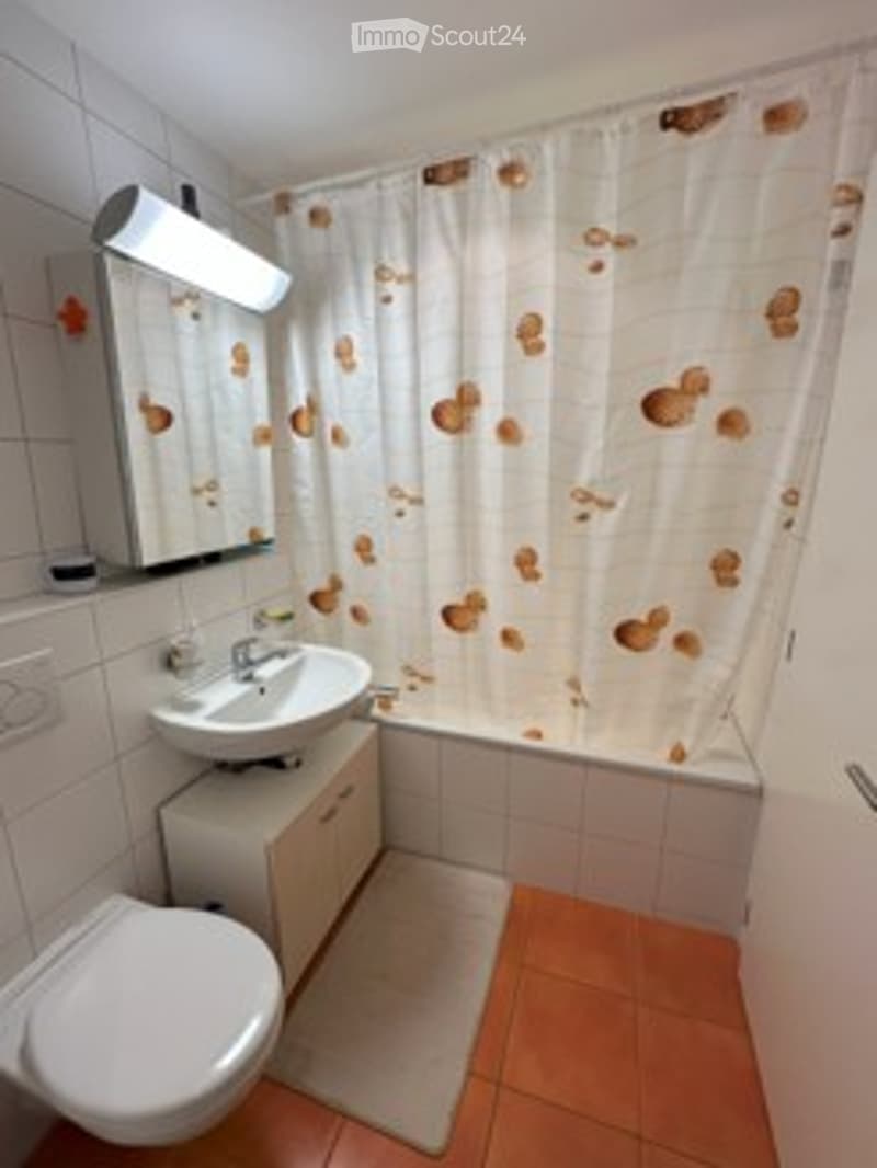 Modern bathroom with white tiles, a sink, mirror, toilet, bathtub, and a shower curtain with a pattern of brown circles.