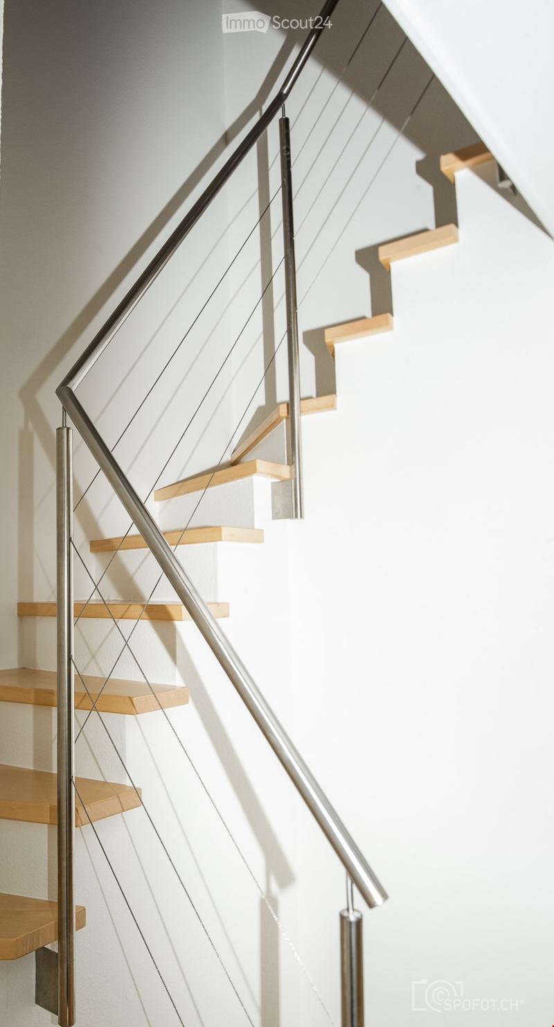 Modern staircase with wooden steps and metal railing, set against a white wall.