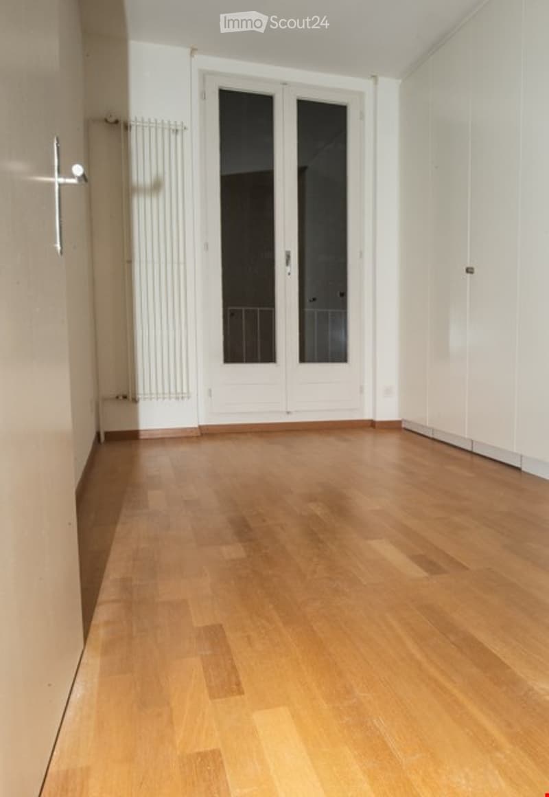 Empty room with wooden flooring, white walls, and a large white door with glass panels leading outside.