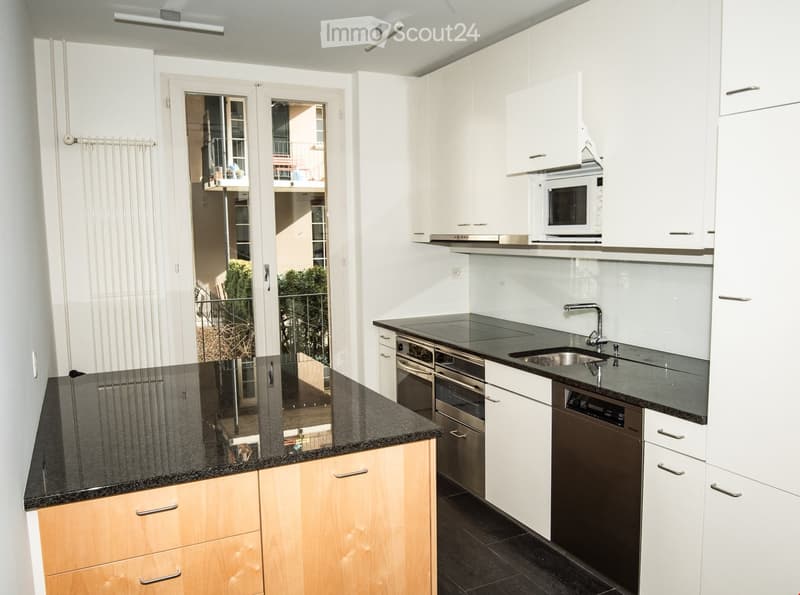 Modern kitchen with white cabinets, granite countertops, stainless steel appliances, and a view to a balcony.