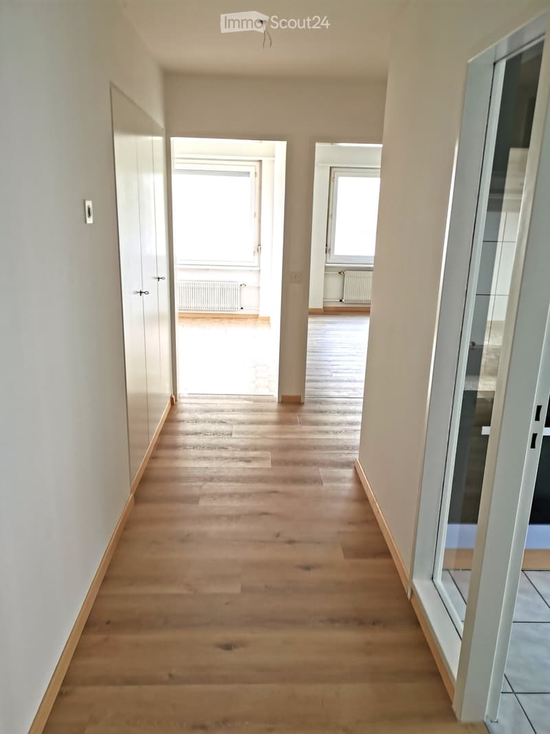 Empty hallway with light wooden flooring, white walls, and several doors leading to other rooms.