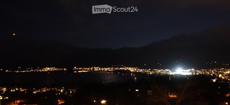 Nighttime view of a cityscape with scattered lights and a dark mountain range in the background.
