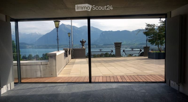 Modern balcony with large glass doors, stone floor, and scenic mountain and lake view.