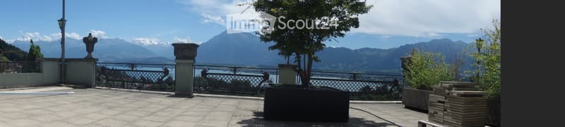 Balcony with a scenic mountain and lake view, featuring a decorative metal railing, stone planters, and a bench.