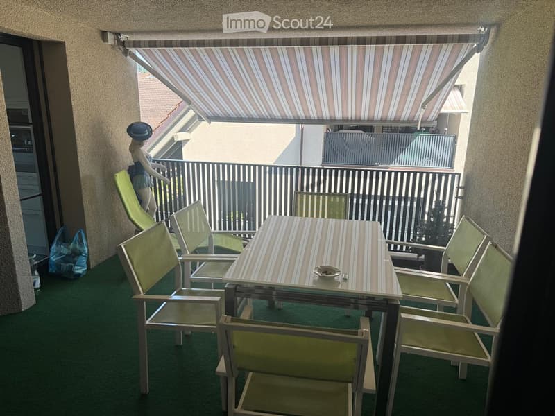 Balcony with green carpeting, a table with chairs, and a decorative statue on the railing.
