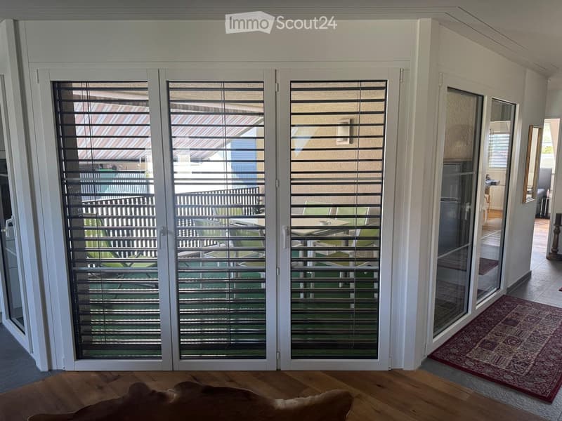 Hallway with large sliding glass doors leading to a balcony or outdoor area, wooden flooring, and a patterned rug visible on the right side.