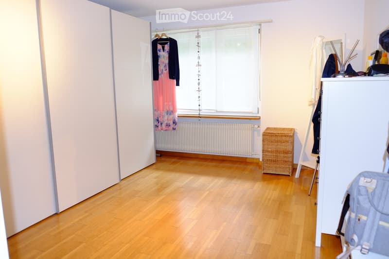 Empty room with wooden flooring, white walls, large window with blinds, radiator, and a small wicker basket near the window.