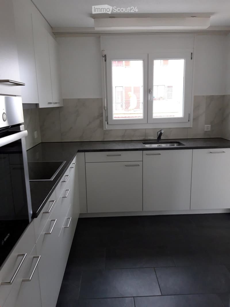 Modern kitchen with white cabinets, black countertops, and stainless steel appliances, including an oven and a sink with a faucet.