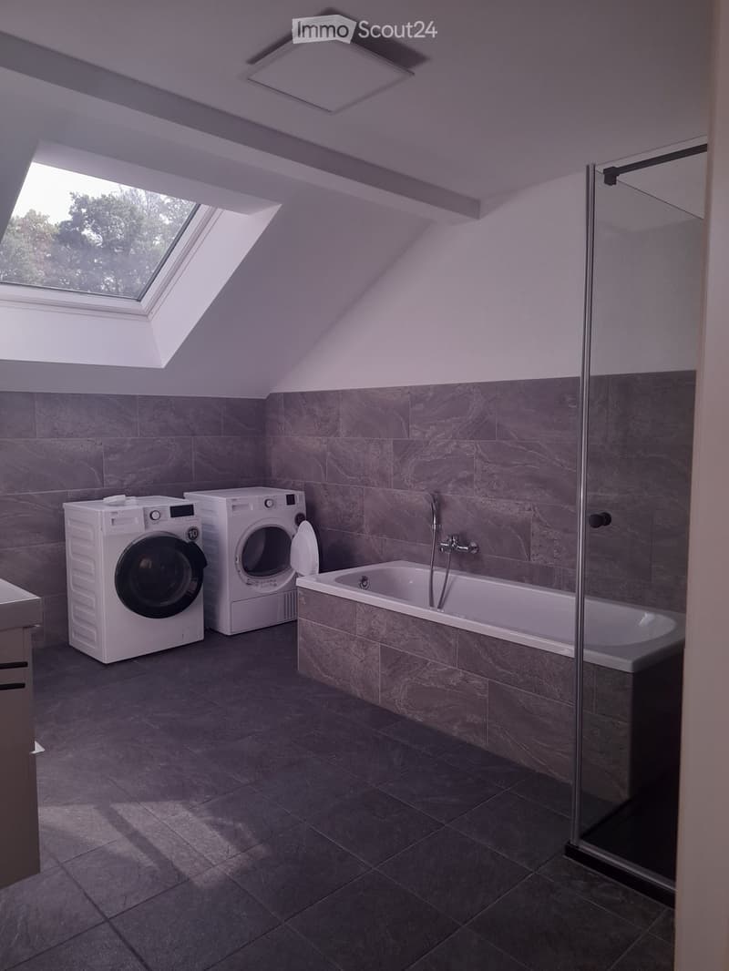 Modern bathroom with a bathtub, washing machine, and skylight window.