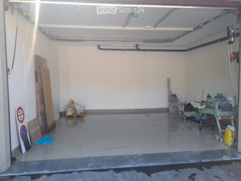 Empty garage with tiled floor, white walls, and scattered items including a ladder, tools, and storage boxes.