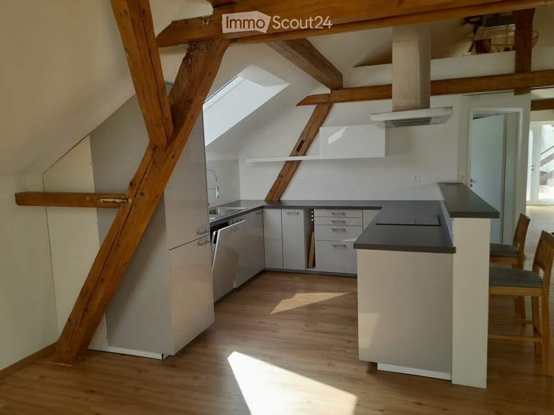 Modern kitchen with light-colored cabinets, stainless steel appliances, and wooden flooring. Features a central island with a black countertop and two stools.