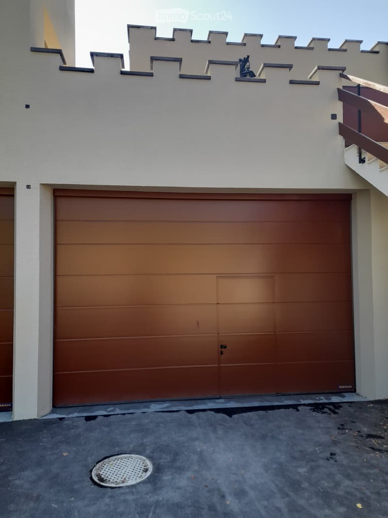 A modern two-story building with a large brown garage door, white walls, and a decorative roofline.