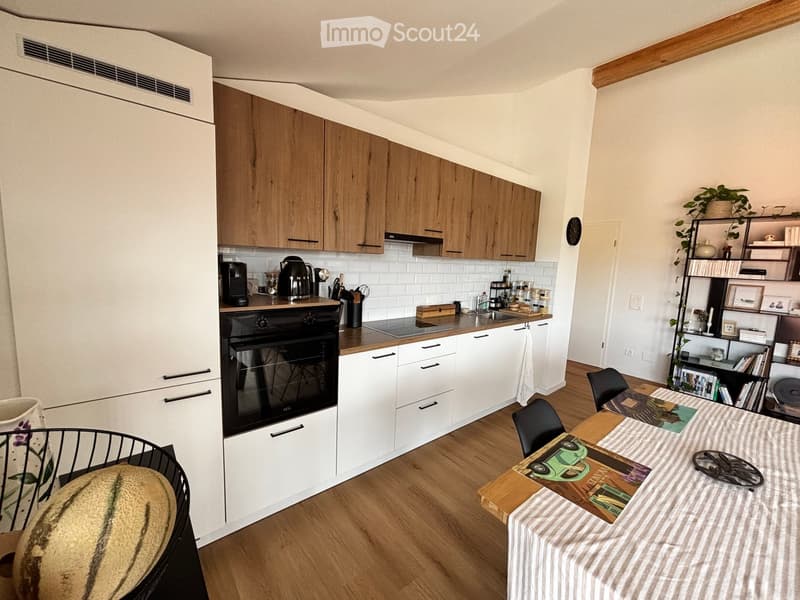 Modern kitchen with white and wooden cabinets, stainless steel appliances, a central island, and a dining area with a table and chairs.