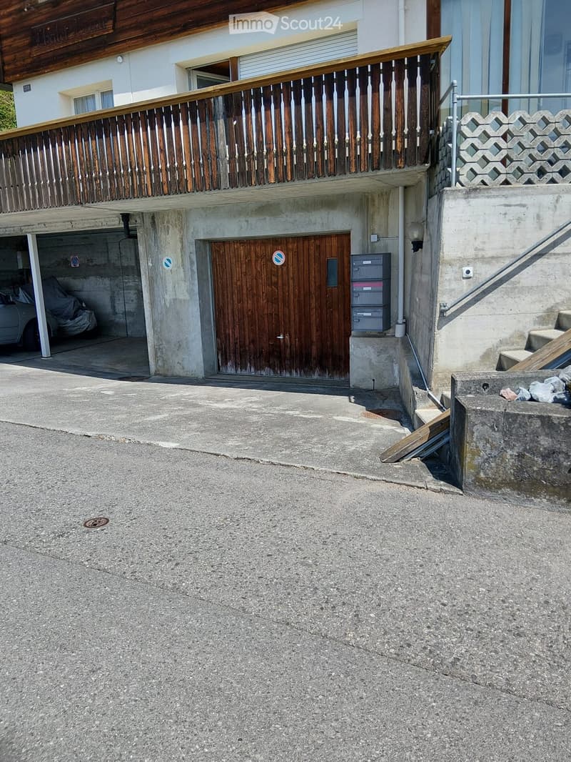 Two-story building with a wooden balcony, garage, and concrete steps leading up to the entrance.
