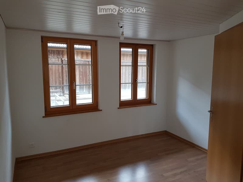 Empty room with wooden flooring, white walls, and two windows with wooden frames. Natural light streams in, and the space is completely unfurnished.