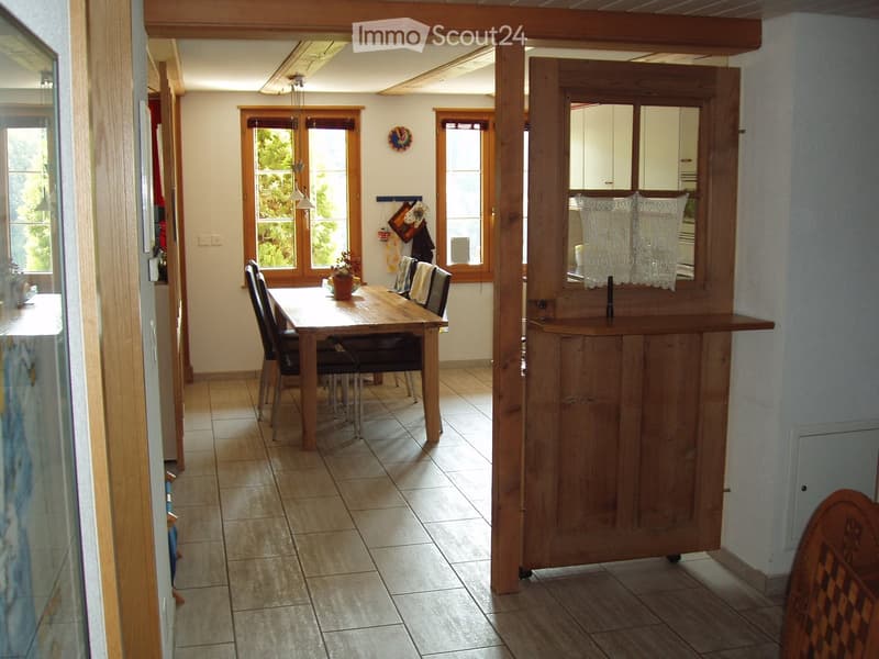 Open-plan dining and kitchen area with wooden dining table, chairs, bar counter, and cabinets.
