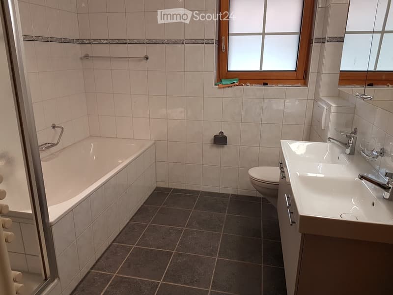 Tiled bathroom with bathtub, toilet, and sink. Wooden window frame and tile flooring.