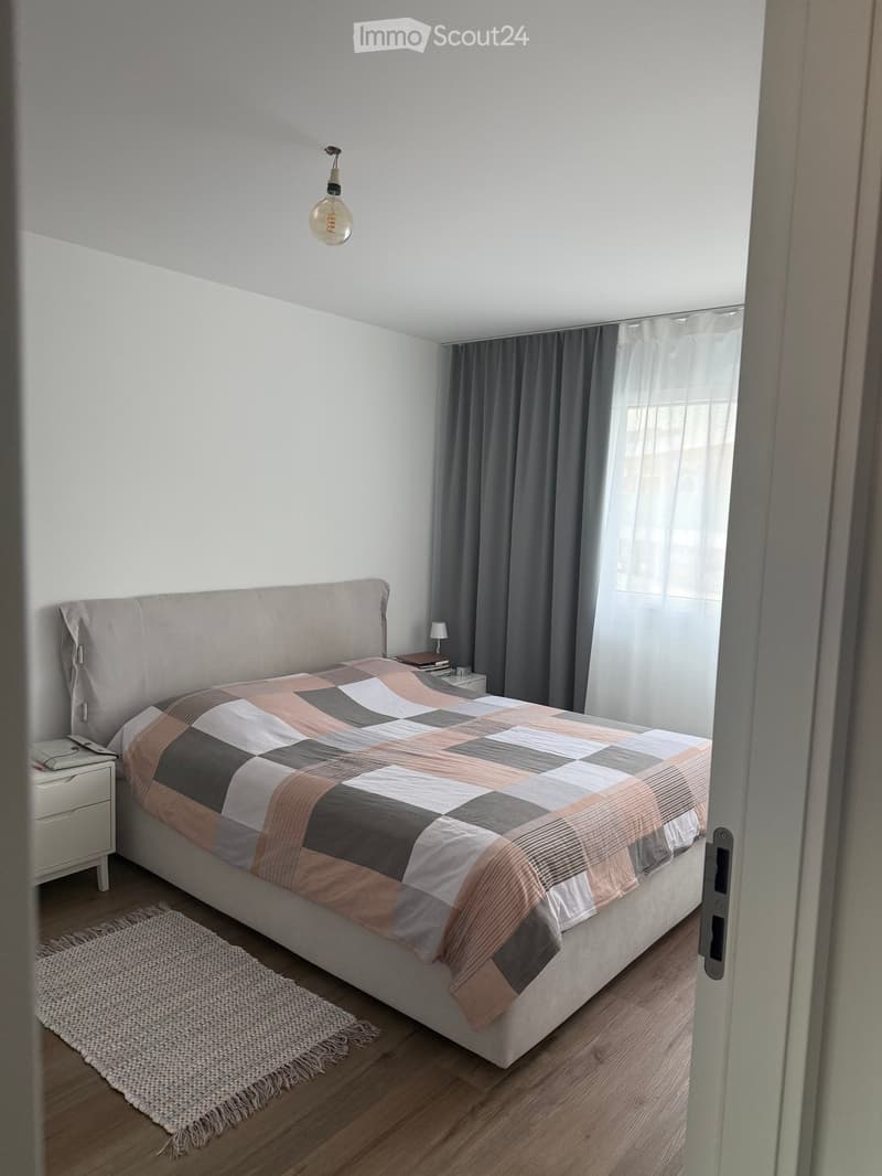 Modern bedroom with a large bed, geometric patterned duvet, nightstand, and a hanging pendant light.