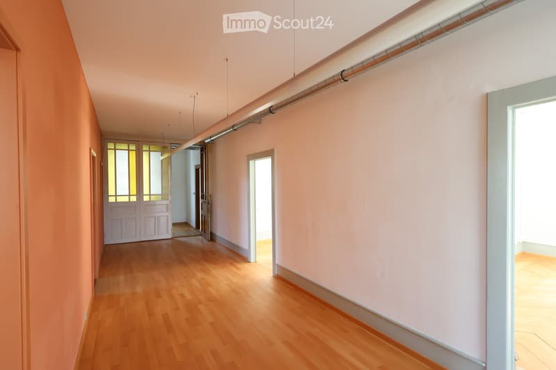 Empty hallway with wooden flooring, white walls, two entrances, and a window on the right side