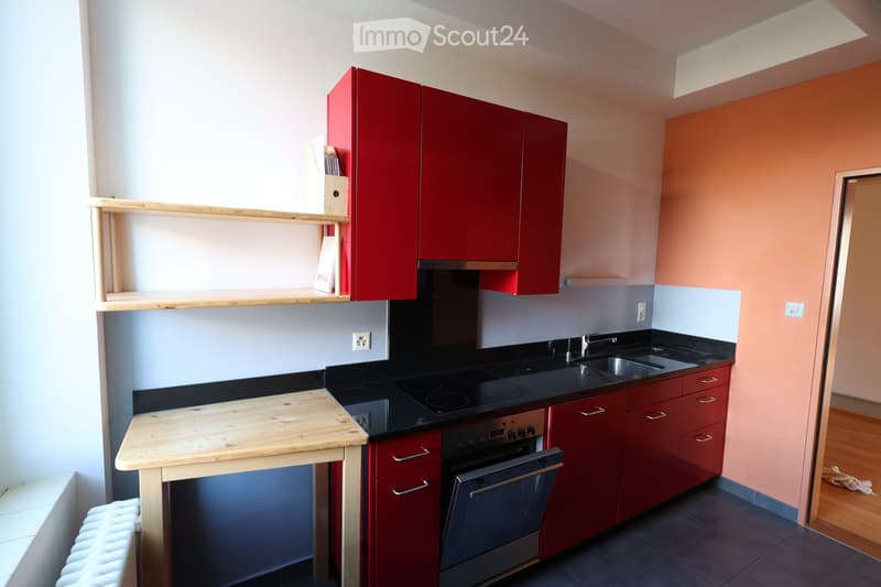 modern kitchen, red cabinets, wooden table, black countertops, stainless steel sink, gas stove, integrated dishwasher, under-counter washing machine