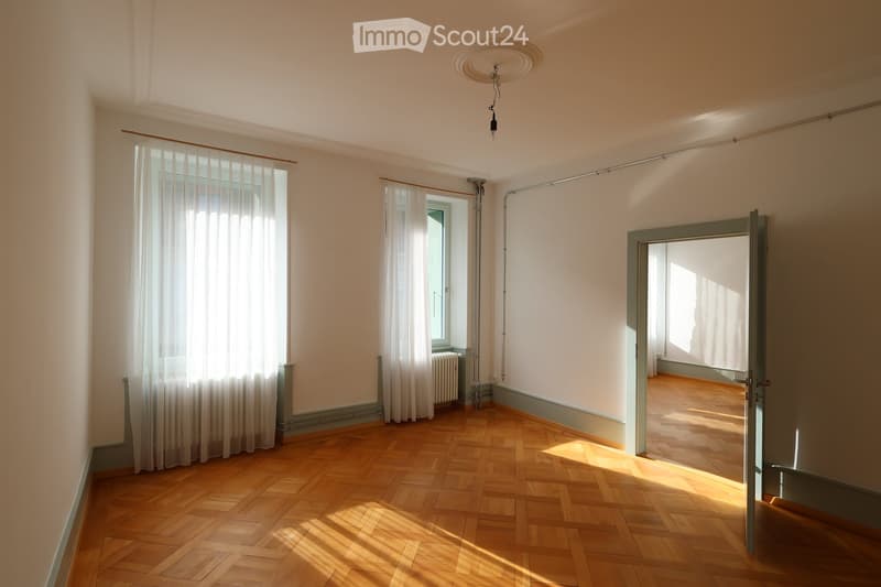Empty room with parquet floors, white walls, white curtains, glass windows, radiator, ceiling lamp
