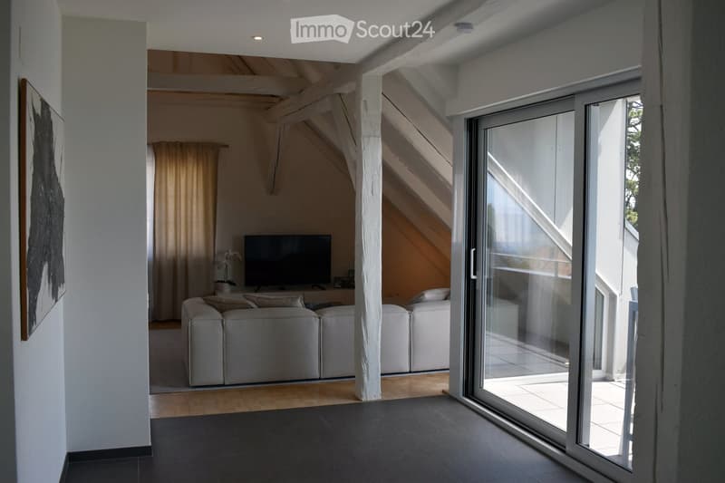 Modern living room with grey sectional sofa, ottoman, flat-screen TV, and a large glass sliding door leading to a balcony.