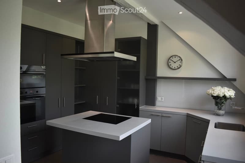 Modern kitchen with grey cabinets, white countertops, induction cooktop, built-in oven, range hood, and a vase with white flowers on the counter.