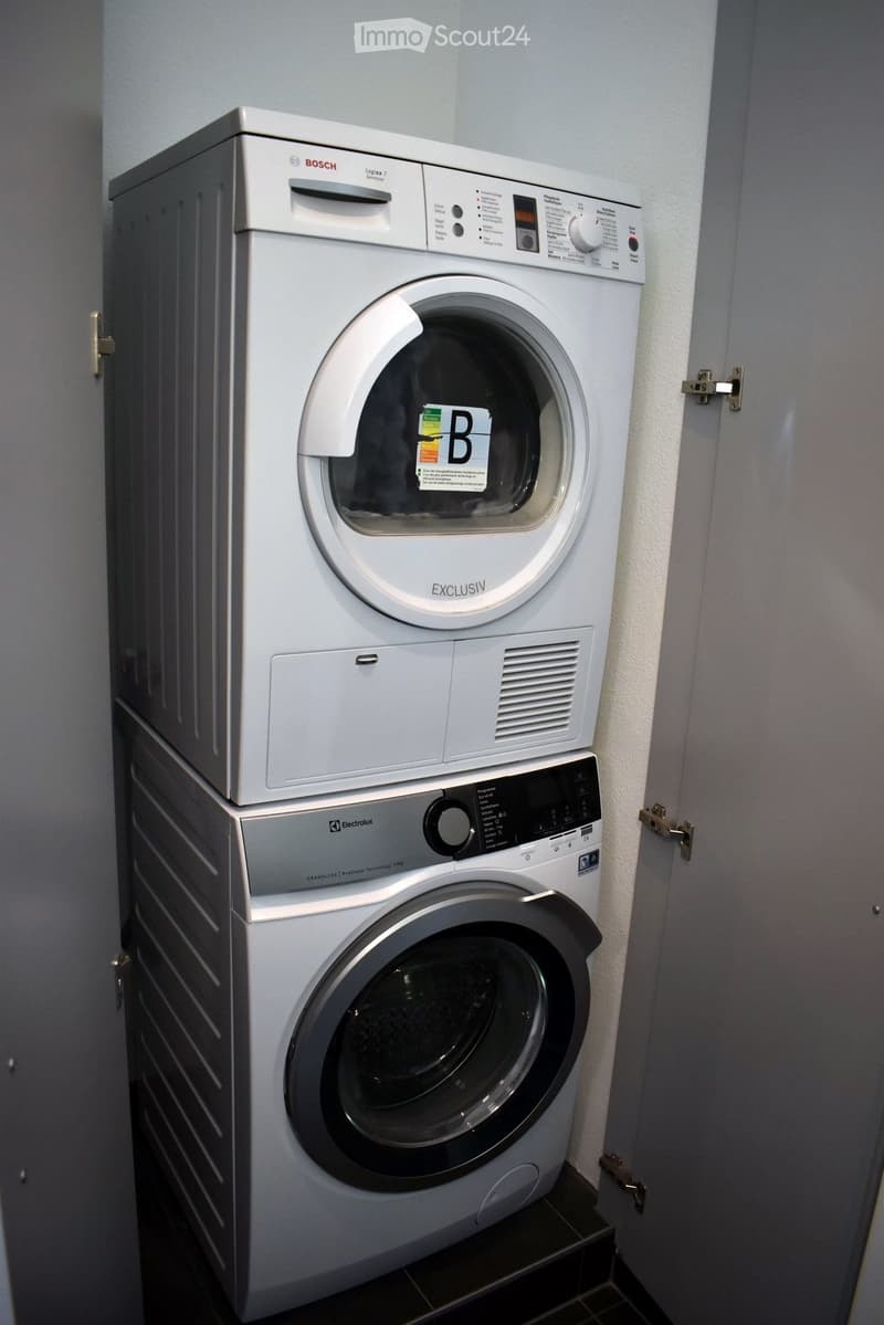 A compact bathroom with a stacked washing machine and dryer unit, both white, against a tiled wall.