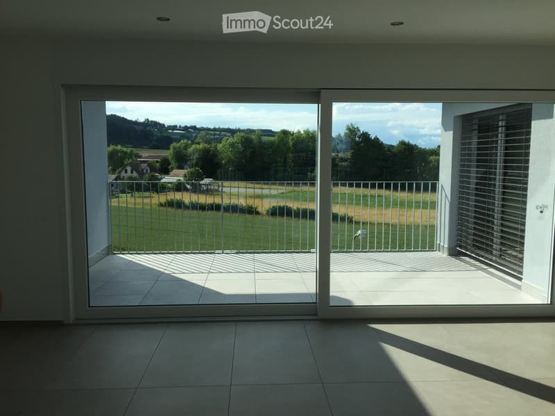 Bright, modern balcony with large sliding glass doors, tiled floor, metal railing, and scenic countryside view.