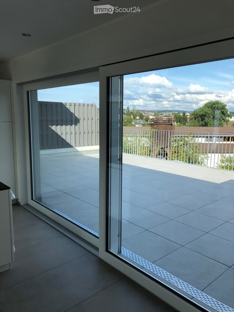 Modern balcony with large glass sliding doors, tiled floor, and a view of the cityscape and surrounding greenery.