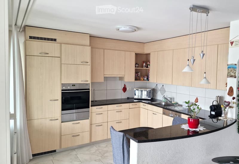 modern kitchen with wooden cabinets, black countertops, stainless steel appliances, hanging lamps, sink, faucet, microwave, toaster, dishwasher, washing machine, potted plant, black and white tiled backsplash