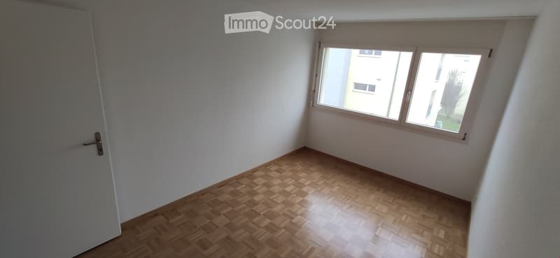 Empty room with wooden parquet flooring, white walls, and a window with white frame. No furniture or equipment present.